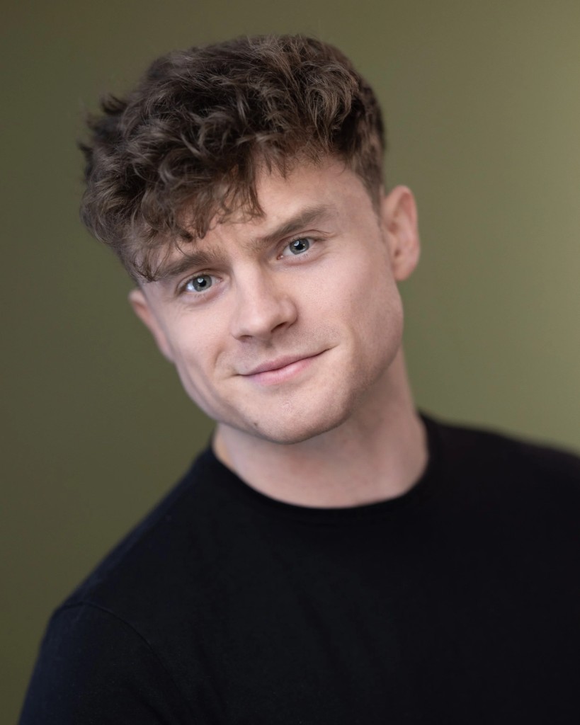 Cormac Brennan, professional headshot with wavy brown hair and black shirt against an olive green background.