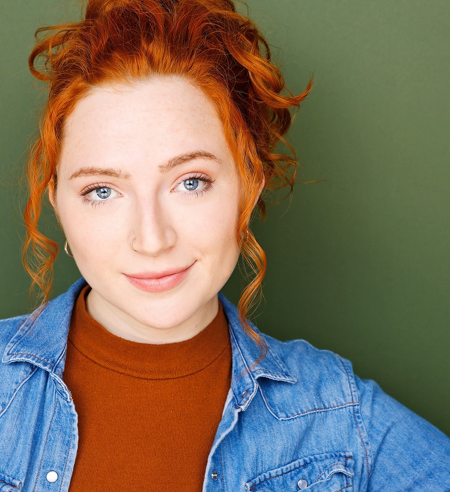 Jessica Fisher, professional headshot with curly red hair, denim jacket, and olive green background.