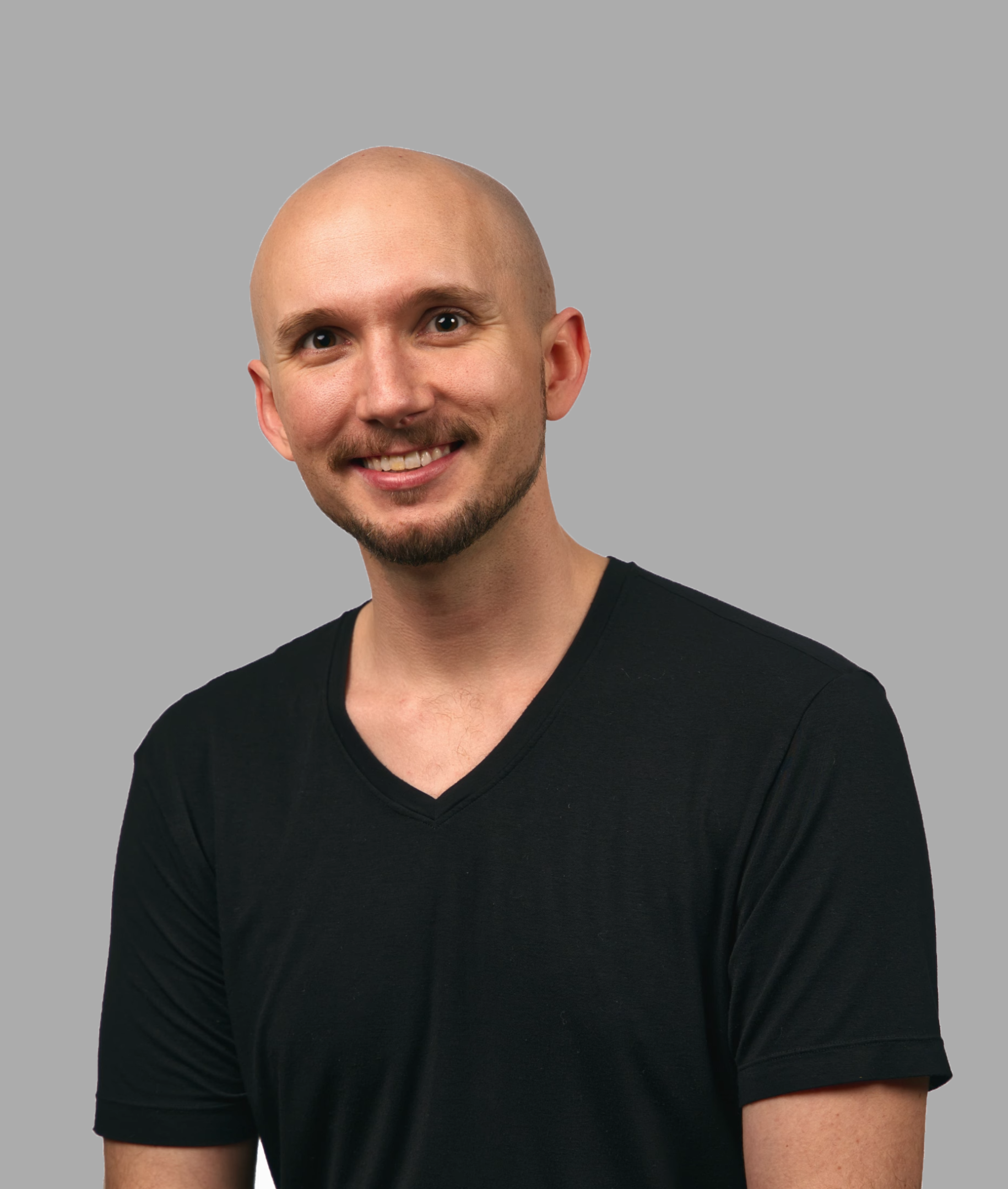 Jesse Nichols, character demo still - smiling, shaved head, black V-neck, light background.